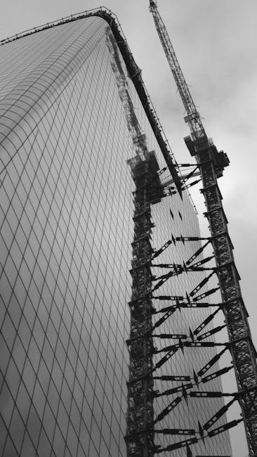 Low angle view of a skyscraper under construction with cranes, captured in monochrome.